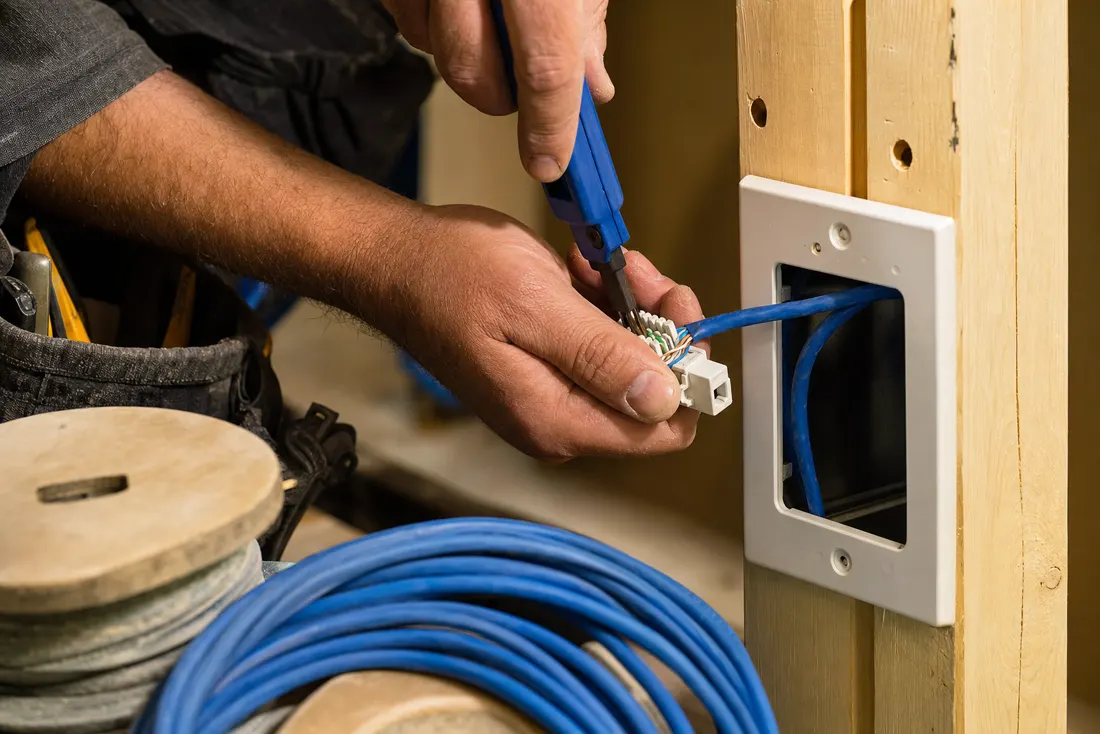 Hands punching down a blue Cat6 cable into a keystone jack at a wall plate