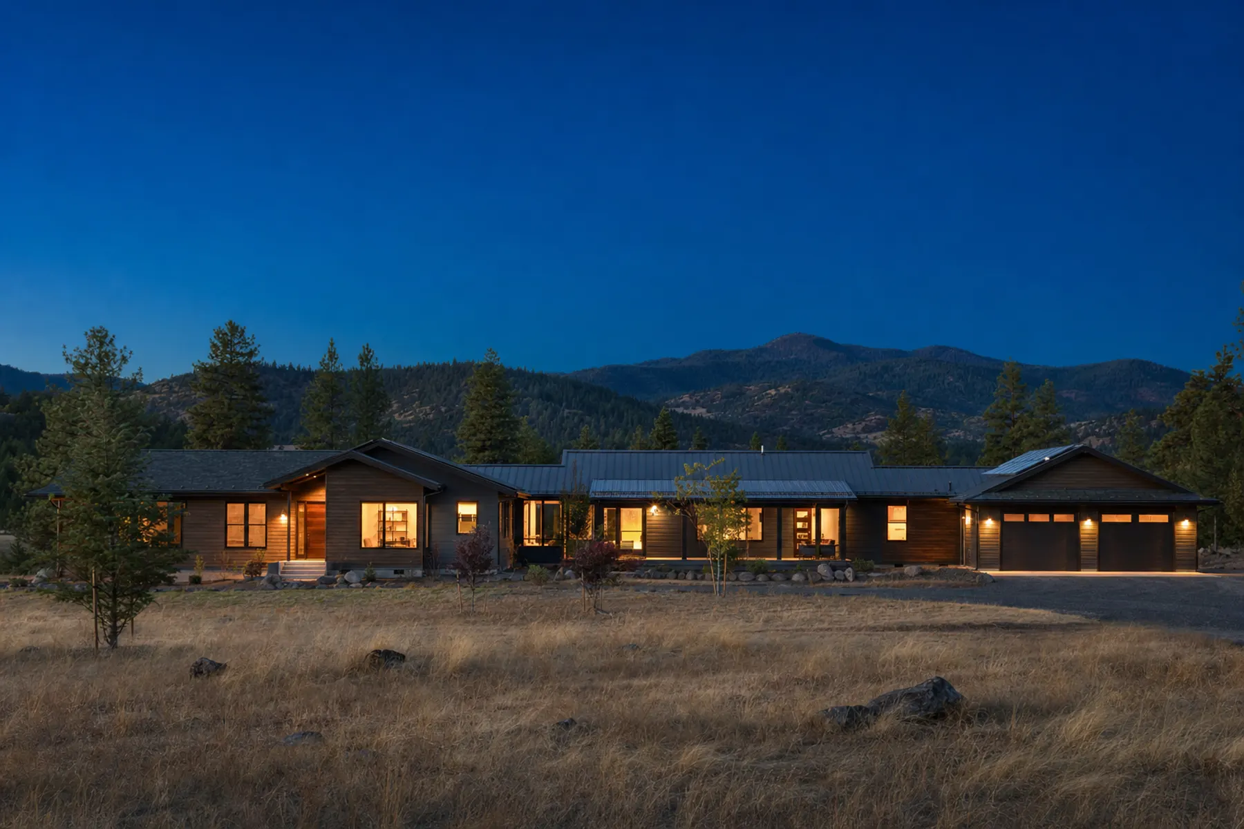 A rural Oregon home lit at dusk with forested hills behind it